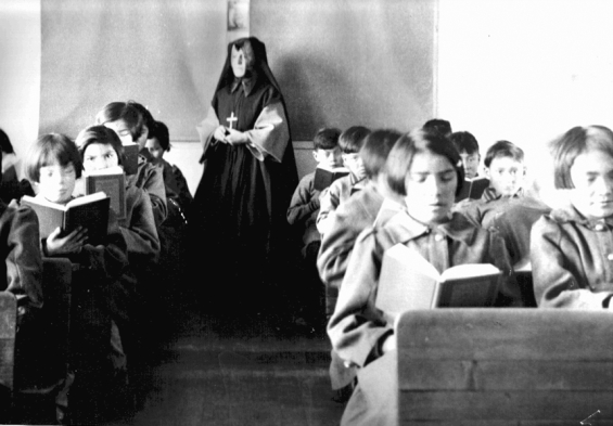 Photograph of students from Fort Albany Residential School reading in class overseen by a nun c 1945. From the Edmund Metatawabin collection at the University of Algoma.